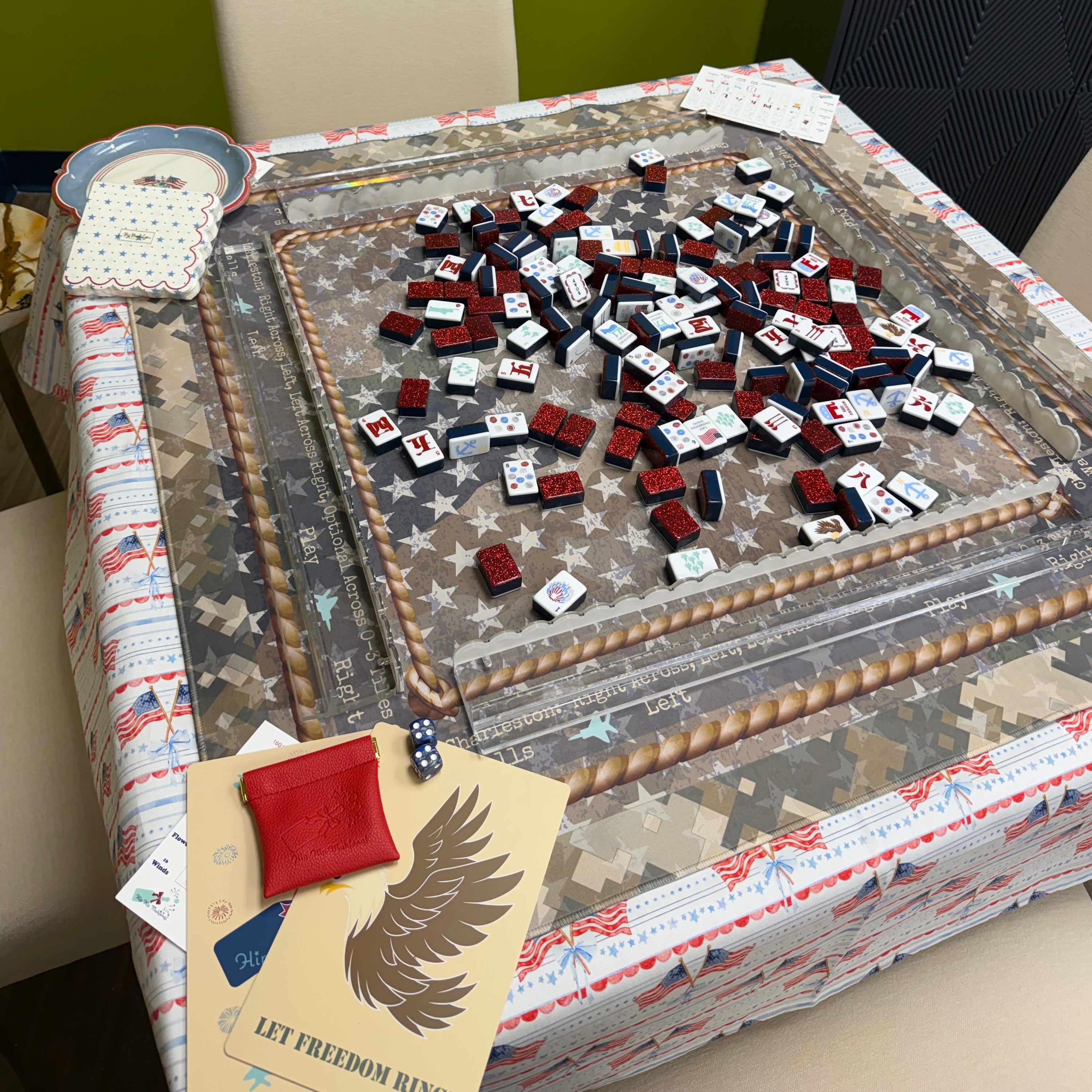 Hexagonal table with a decorative cover featuring American flags and stars, surrounded by framed pictures on a green wall.